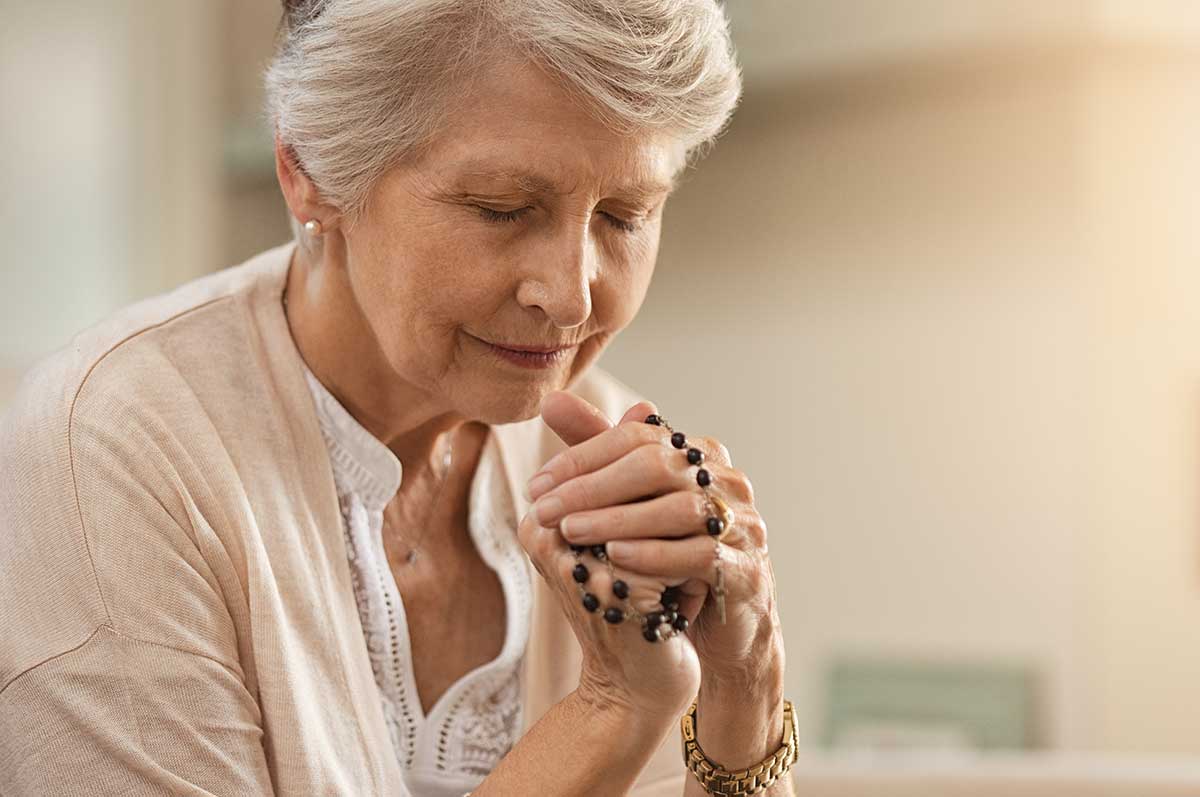 senior woman praying and holding rosary beads
