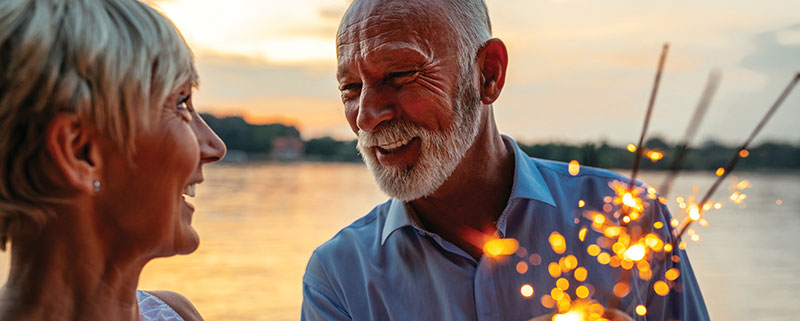 Senior couple smiling at each other using sparklers on waterfront