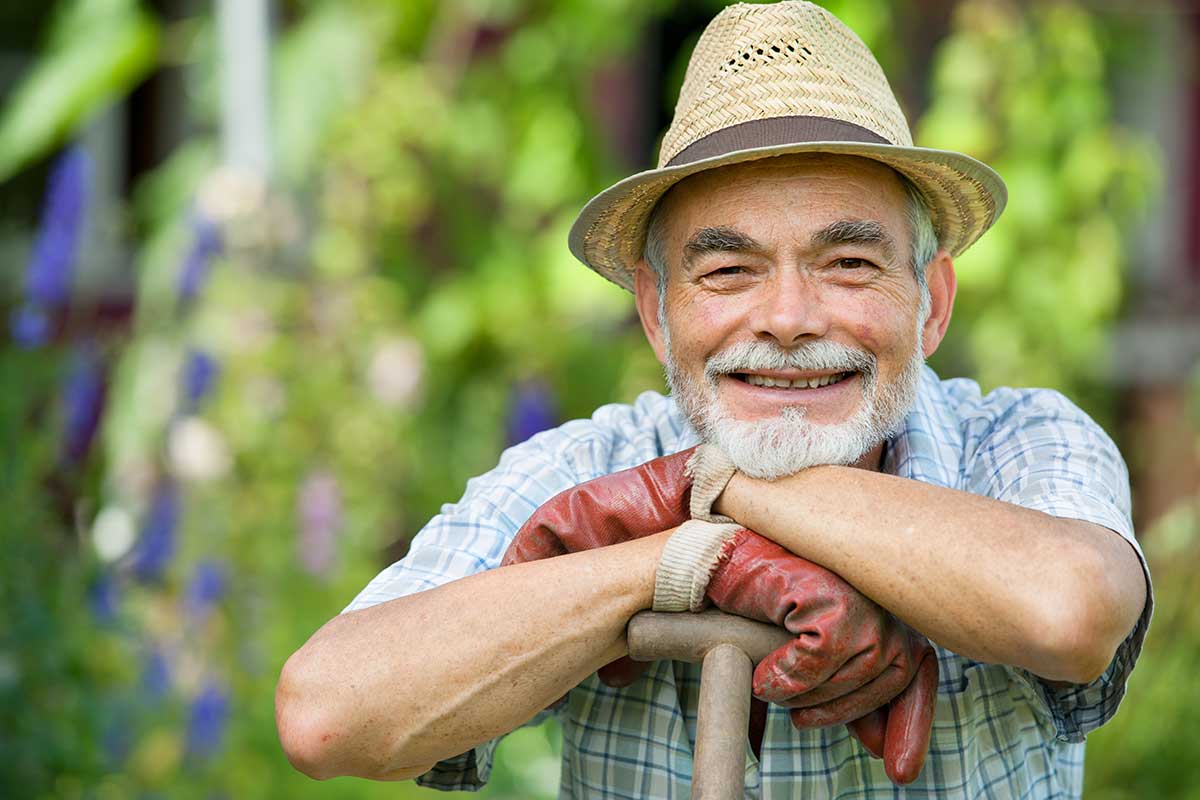 senior man gardening wearing hat and gloves and resting on shovel handle