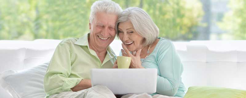 2 seniors, a man and a woman, laughing while looking at the computer screen