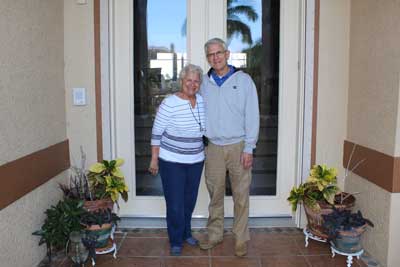 Elderly couple standing in front of their house smiling
