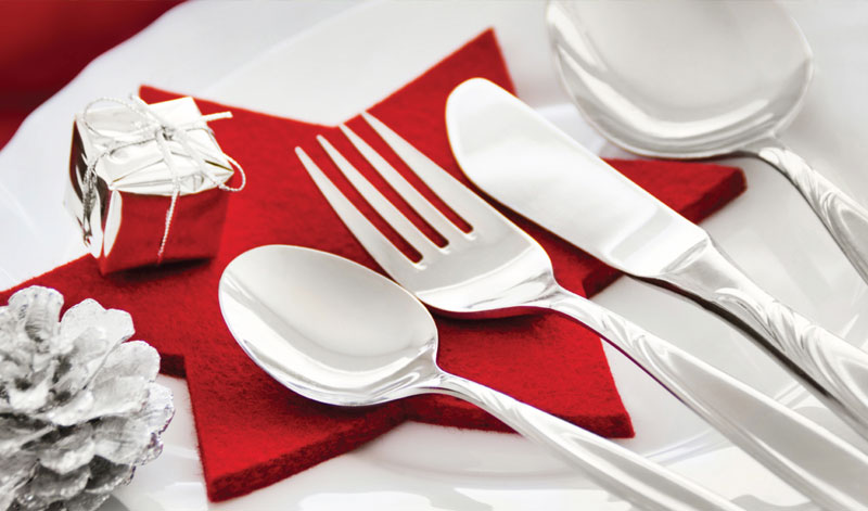 A place setting with silverware, a small wrapped gift, and a pinecone on a red star-shaped napkin.
